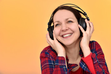 Happy smiling beautiful woman with headphones listening to music, resting and enjoying. Isolated on the orange background.