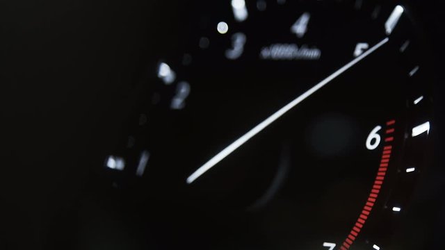 Car dashboard. Black, white numbers and arrows. Night, interior lighting. Tachometer, speedometer, sharp, fast acceleration of the car forward. The arrow rises quickly to the red zone, cutoff