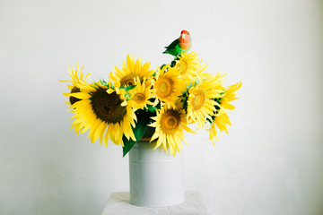 bouquet of bright yellow sunflower flowers with a lovebird parrot in a retro vase on a white background