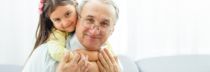The happy girl hugs a grandfather on the sofa