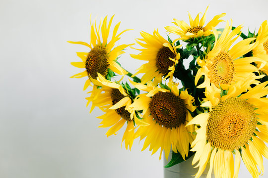bouquet of bright yellow sunflower flowers in a retro vase on a table covered with a white tablecloth on a white background