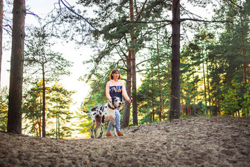 Woman and great Dane dog walking and looking away in forest