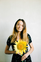 a young pretty girl in a black floral dress holds a vase of sunflower flowers on a white background