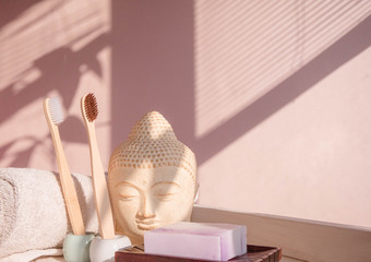 White Buddha bust on pastel pink background decorated with shades. Zero waste bamboo toothbrush. Spa asian style. Relax mood. Yoga background. Eco friendly