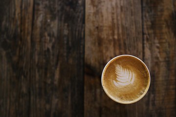 Coffee cup with decorative leaf design in on rustic wood background - top view with space for text