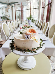 a white cake decorated with flowers and herbs stands on a wooden table in a restaurant at a wedding.