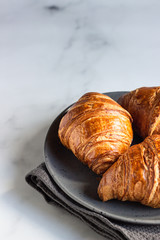 Three delicious fresh croissants on a ceramic plate, light grey background. 