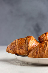 Three delicious fresh croissants on a ceramic plate, light grey background. 