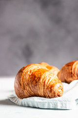 Fresh croissants on a grey linen napkin. Light grey concrete background. 