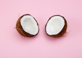 Fresh raw coconut cut into 2 parts on a pink background.
