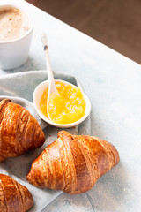 Fresh croissants on a grey linen napkin with jam and coffee. Light grey concrete background. 