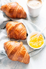 Fresh croissants on a grey linen napkin with jam and coffee. Light grey concrete background. Top view.