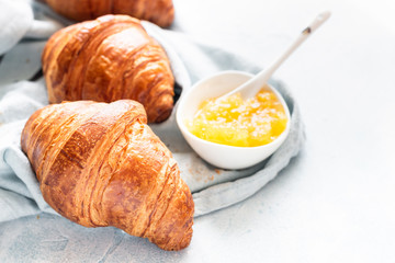 Three delicious fresh croissants on a ceramic plate, light grey background. 