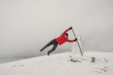 Man in red coat being blown off a mountain by wind