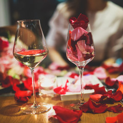 Beautiful glass with rose leafs, rose-petal, rose petals on a romantic date with wine, candles in candlelight and with celebrating couple on the background, interior for a romantic date diner