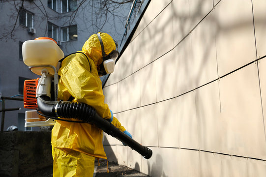 Paramedic Wearing Yellow Protective Costume And Mask Disinfecting Coronavirus With The Motorized Backpack Atomizer And Sprayer