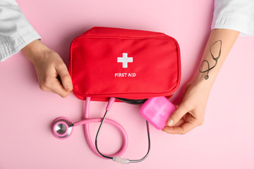 Hands of doctor with stethoscope and first aid kit on color background