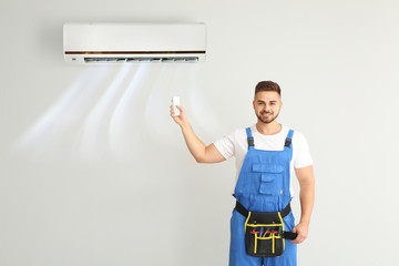 Male technician switching on air conditioner on light wall
