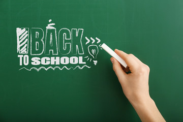 Woman writing phrase BACK TO SCHOOL on blackboard in classroom