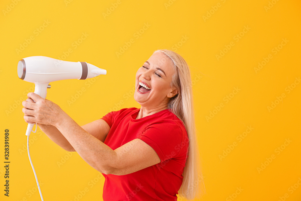 Wall mural Beautiful mature woman with hair dryer on color background