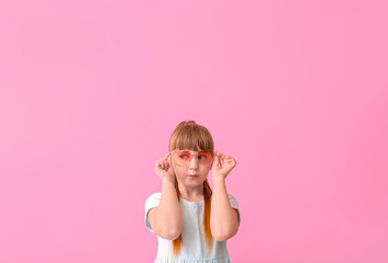 Funny little girl with sunglasses on color background