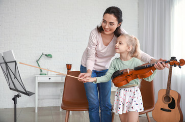 Private music teacher giving violin lessons to little girl at home