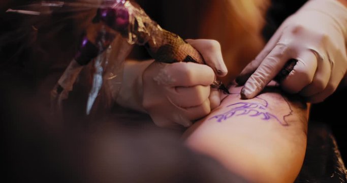Tattoo artist making a tattoo of a deer on a person's hand. Close up, slow motion, shallow depth of field. BMPCC 4K
