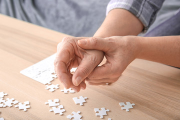 Senior woman suffering from Parkinson syndrome doing puzzle at home