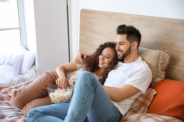 Happy young couple watching movie in bedroom