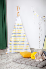 Interior of modern children's room with yellow teepee. Children wigwam home. Interior of stylish children's room with toys. scandinavian style. Kids room with a beautifully decorated play tipi tent. © stock_studio