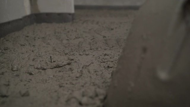 A construction worker with a shovel throws the mortar onto the floor. Spread the mortar on the concrete floor with a shovel. Flooring. Laying mortar on a concrete floor.