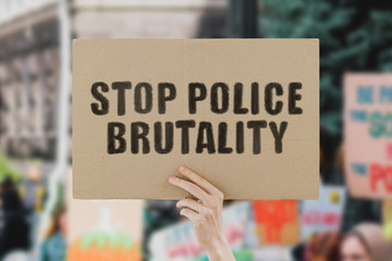 The phrase " Stop police brutality " on a banner in men's hand. Human holds a cardboard with an inscription. Power. Government. Rally. Protest. Crowd. Street. Urban. March. Dictator. People