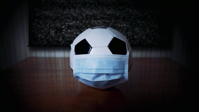 The ball in the medical mask near the idle TV. Football match canceled. World epidemic. Cancel mass events. Cancel, reschedule football championship. Coronavirus. TV without image. Upset fans. Glitch