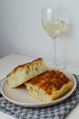 Traditional italian bread, focaccia siciliana with sardines, tomatoes and oregano, glass of white wine in the background