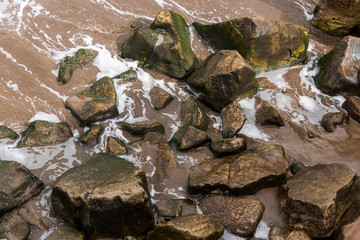 Moving water with white foam between the rocks of the shore