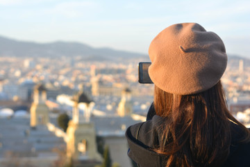 Fototapeta premium Fashion tourist girl with a hat on her back taking pictures with her smartphone to a city.Barcelona. Concept: tourism, travel, vacations