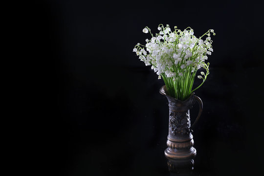 A small bouquet of lilies of the valley in an old vase. Photo on a black background.