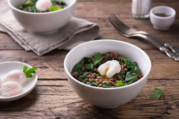 Boiled lentils with spinach, herbs, spices and poached egg in ceramic bowls on a wooden background. Simple healthy homemade food