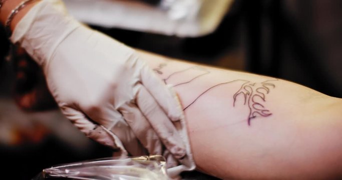 Tattoo artist sprinkles sterile liquid on a person's hand with a tattoo. Slow motion, shallow depth of field. BMPCC 4K