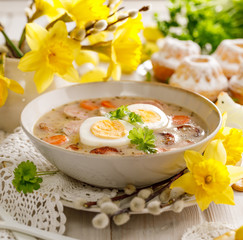The sour soup (Żurek), polish Easter soup with the addition of sausage, hard boiled egg and vegetables in a ceramic bowl, close up.  Traditional Easter food in Poland - 328396756