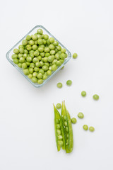 Chicharos  pelados en un recipiente de cristal con unos chicharos con cascara a un costado sobre un fondo blanco