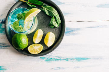 Refreshing drink with lime. Homemade mojito on summer wooden table surrounded by limes, peppermint and sugar. Copyspace
