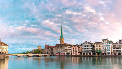 Fototapeta premium Famous Fraumunster church with its reflections in river Limmat at pink sunrise in Old Town of Zurich, the largest city in Switzerland