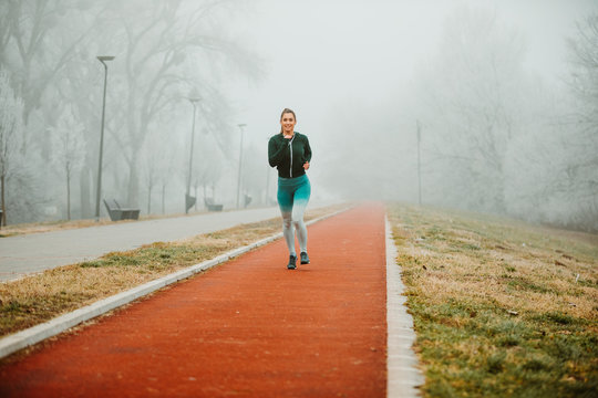 Photo of young sportive girl wearing sportswear while jogging outside on foggy morning.