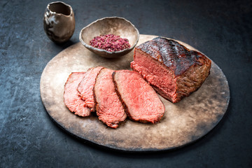 Traditional Commonwealth Sunday roast with sliced cold cuts roast beef with red salt as closeup on a modern design plate with copy space