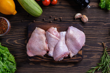 Fresh raw chicken drumstick and thigh on a board with spices and herbs on a wooden table