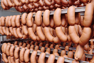 Sausages hanging in a smoking chamber close-up against a meat-packing plant