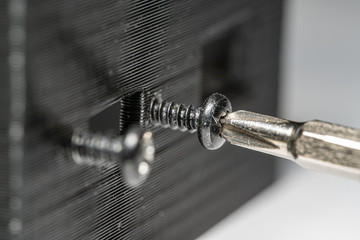 Macro photo of a small screwdriver being used to screw a small screw into a 3D printer part