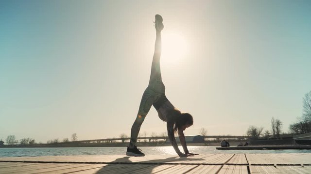 young athletic girl with a great stretch is the splits on on the background of a beautiful sunset and lake. Slow motion