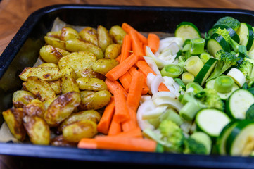 Cooking tray with green vegetables, carrots and patatos on wooden kitchen table